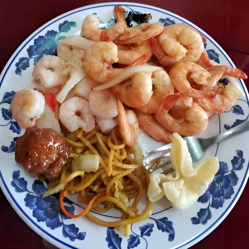 A buffet plate filled with shrimp, lo mein, a crab rangoon, and a sweet and sour chicken ball.