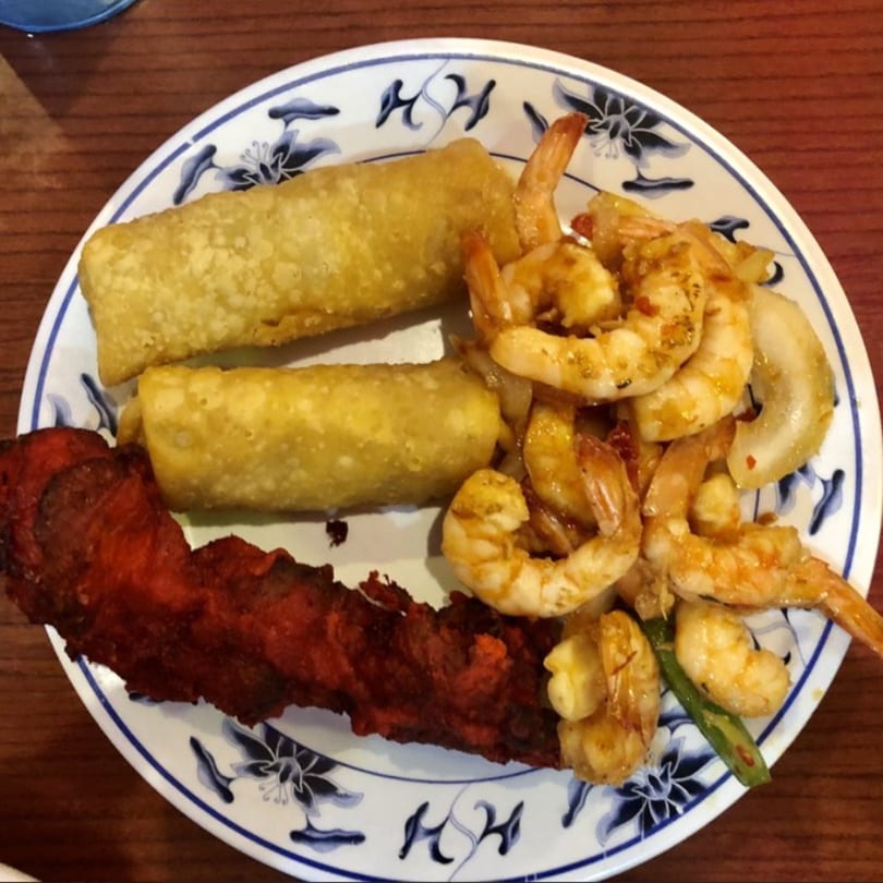 A buffet plate with two egg rolls, a large piece of red meat, and seasoned shrimp with onions.