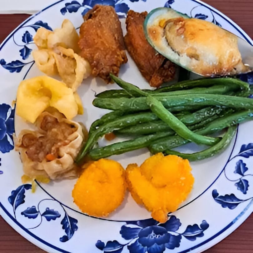 A blue and white plate filled with Asian Garden Buffet items, including fried chicken, mussels, green beans, and dumplings.